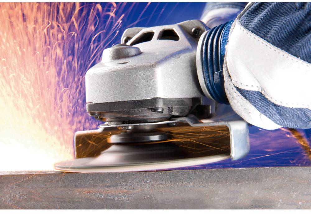 A person is grinding metal with an angle grinder. Sparks are flying from the disc. Protective gloves and protective clothing are visible.
