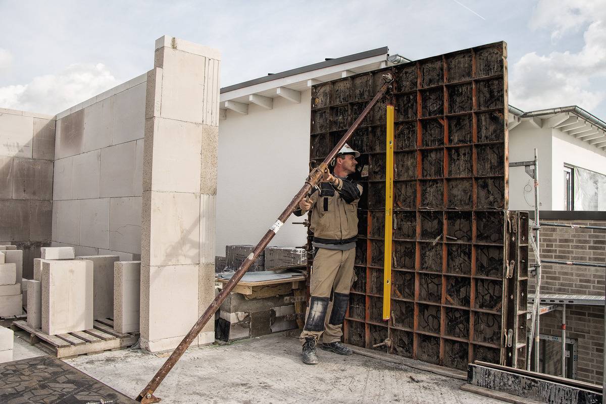 A construction worker is positioning formwork at a building site. Unfinished walls and tools can be seen around him.