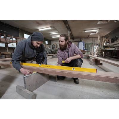 Two men in work attire are checking the level of a piece of wood using a spirit level in a woodworking workshop.
