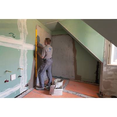 A craftsman is aligning a plasterboard wall in an attic using a spirit level. Working materials are lying on the floor.