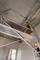 A person is working at the top of a scaffolding in a room with unplastered walls.