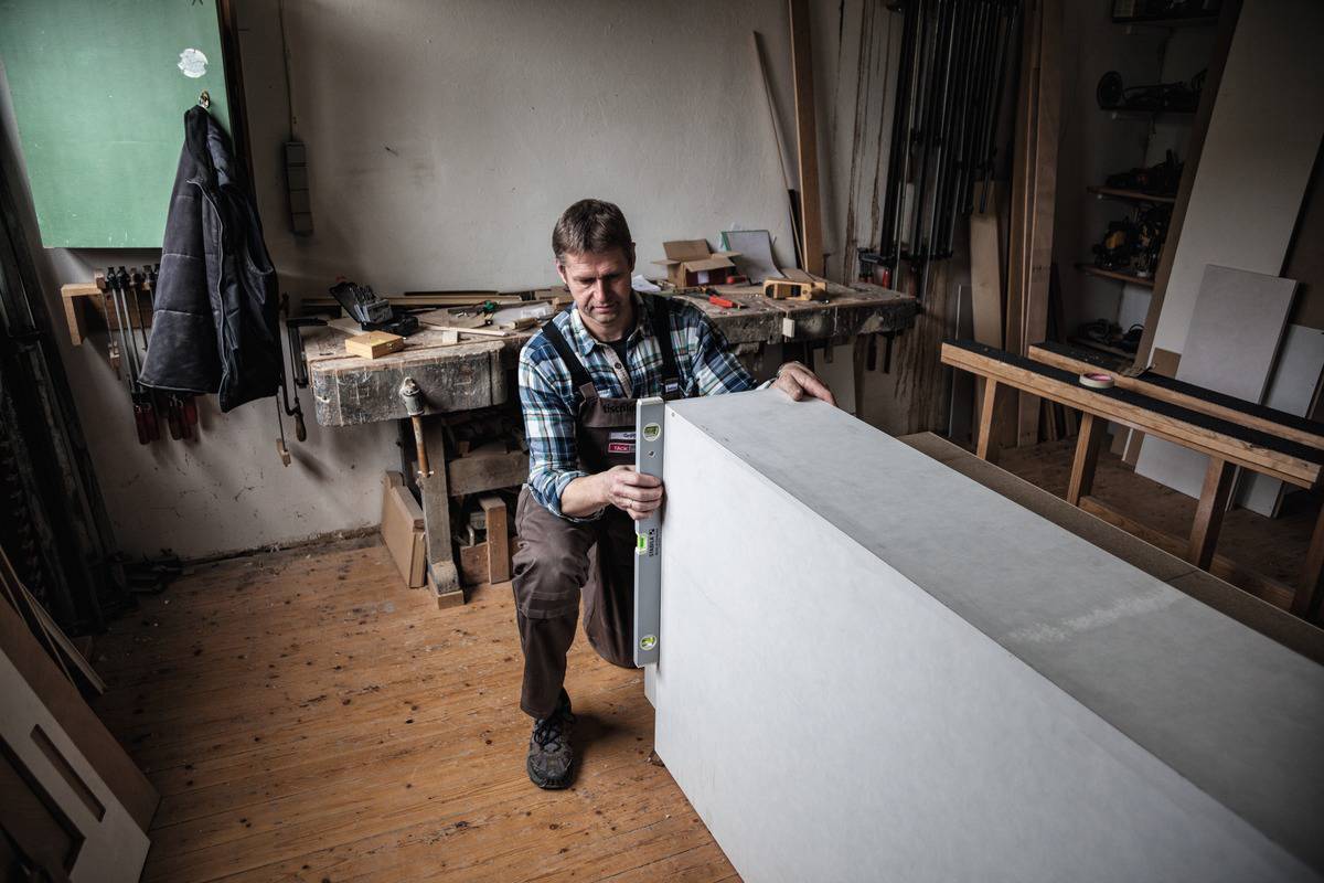 A man in a workshop is using a spirit level on a large block to check its alignment.
