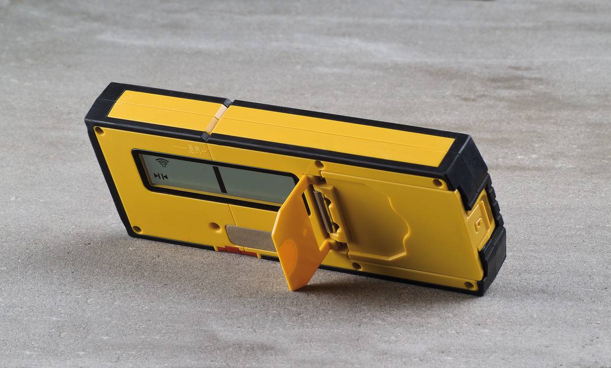 A yellow electronic device with a display and fold-out stand is positioned at an angle on a surface. It is used for measurement.
