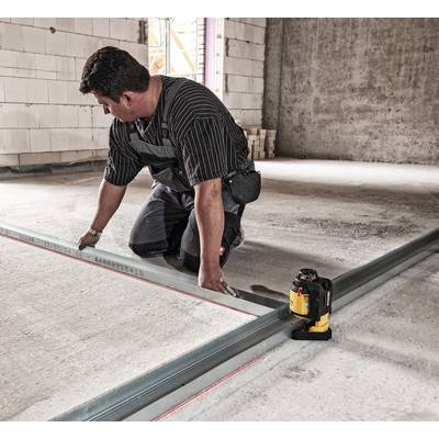 A man is aligning metal strips on a concrete floor, assisted by a yellow laser tool for precise positioning.
