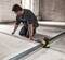 A man is aligning metal strips on a concrete floor, assisted by a yellow laser tool for precise positioning.