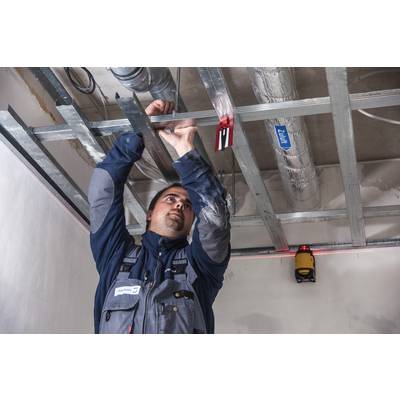 A tradesman in workwear is installing metal profiles on a ceiling. He is using a spirit level to align the construction.