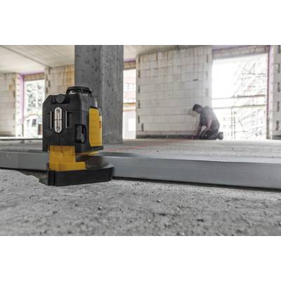 A rotating laser on a construction site projects a line onto the ground, while a worker in the background takes measurements.