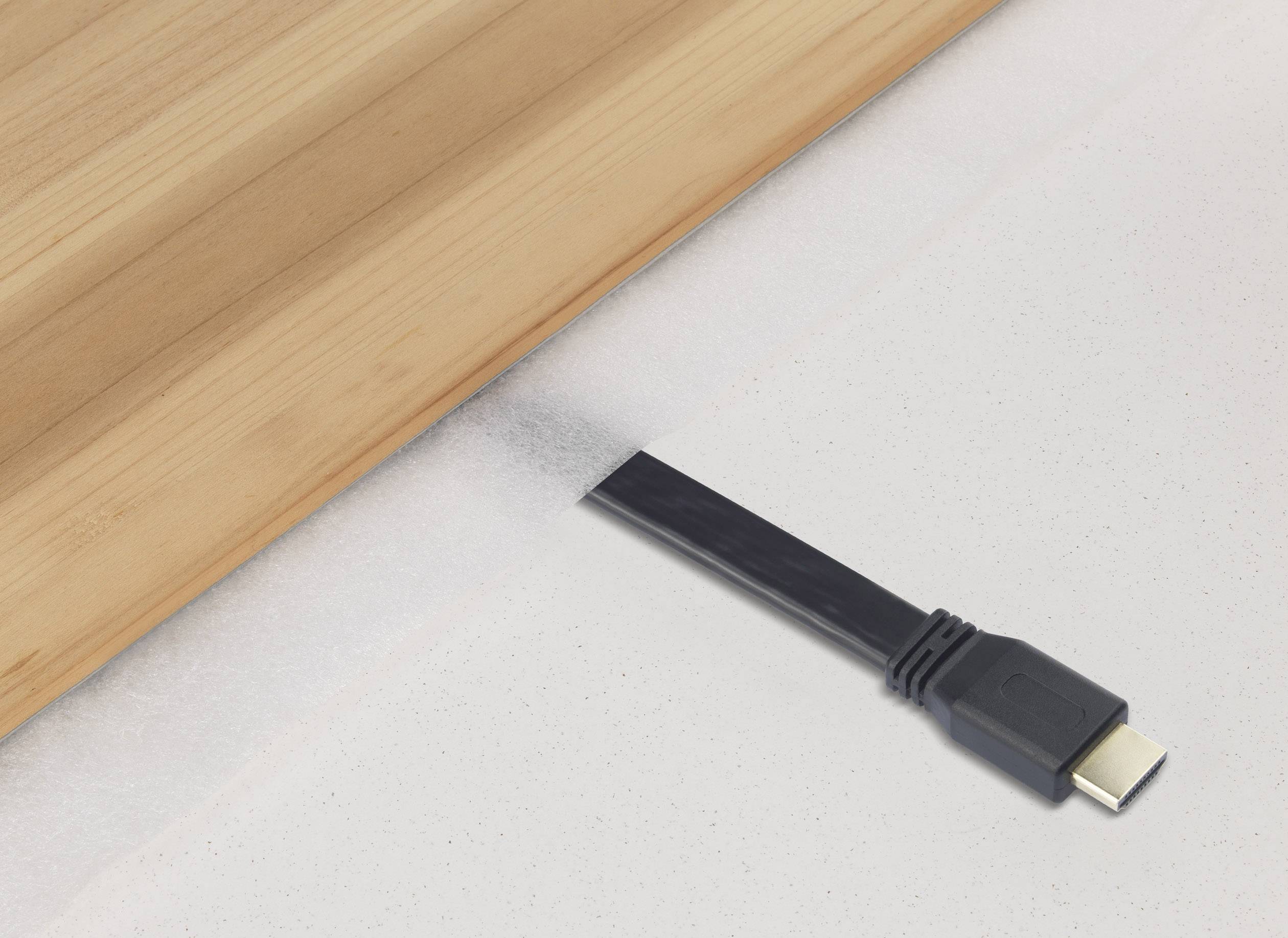 A black HDMI cable lies on a light-coloured floor, with its end partially hidden beneath a wooden floor.