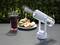 Small fan expels vapour, while a wasp flies near a plate of food and a glass of red liquid outdoors.