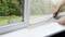 A person is cutting a transparent protective film along a window frame. A garden is visible in the background.