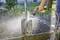 A person is cleaning a dirty spade with a hosepipe in a garden. Water droplets are splashing into the air.