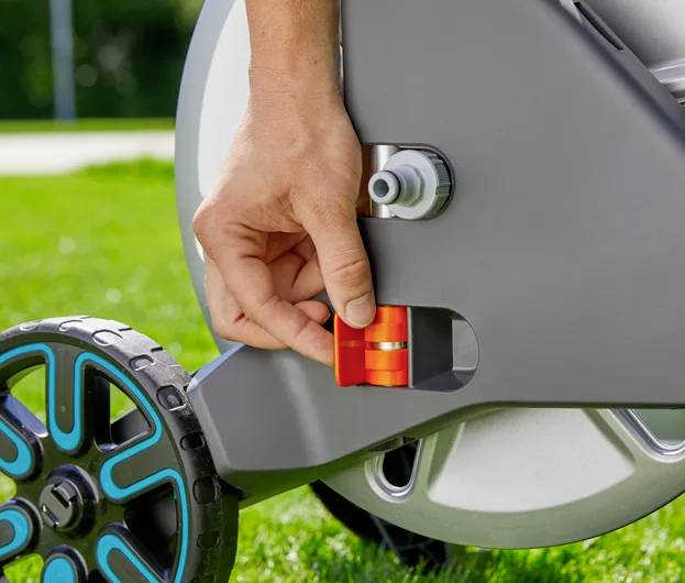 A person adjusts the height of a lawn mower wheel on a sunny day, showcasing an easy-to-use mechanism for modifying grass cutting height.