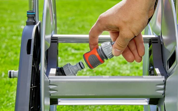 A hand connects a garden hose to a reel on a green lawn, demonstrating setup for outdoor watering.