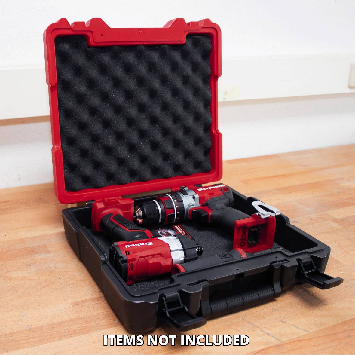 A black tool case with a red trim, containing drill drivers and batteries. Text 'Items not included' on the floor in front of the box.
