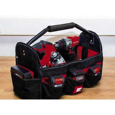 A black tool bag with various red power tools and batteries on a wooden table.