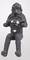 A sculpture depicts a small, black figure holding an electronic device. The figure is seated and intricately designed.