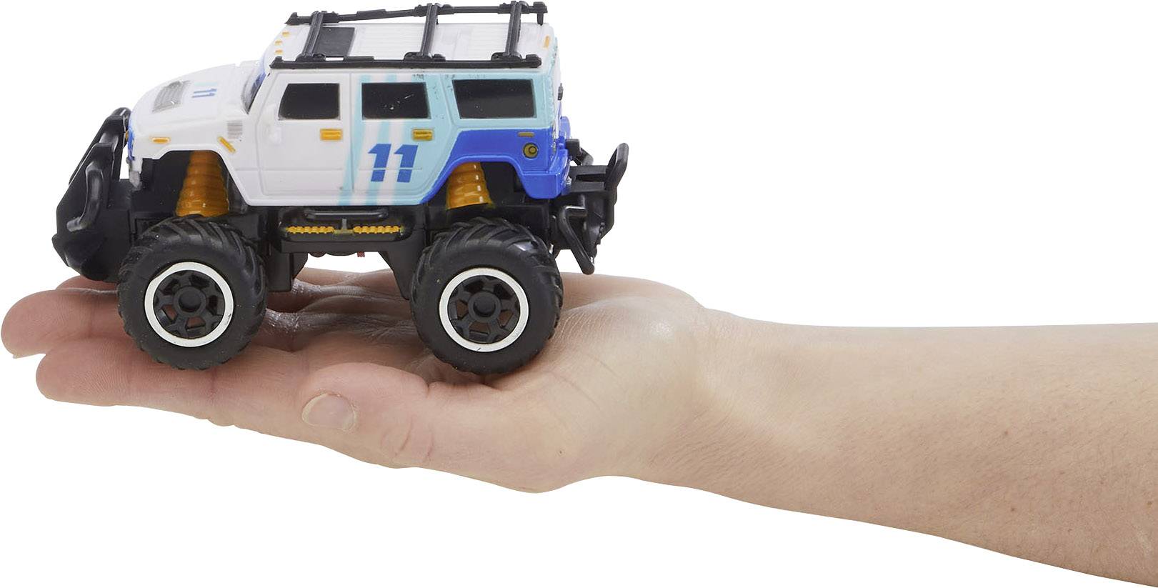 A white and blue toy monster truck model with the number '11' sits on a hand. The truck has large tyres and orange shock absorbers.