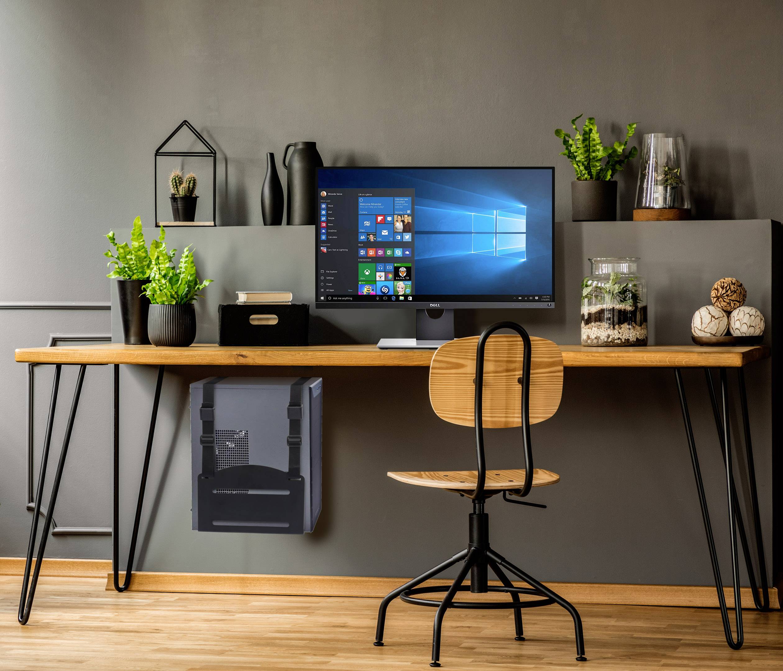 Modern desk with a monitor displaying Windows 10. Plants and decorations on the shelving, a wooden chair in front.