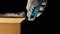 A gloved hand uses a cutting tool to trim the edge of a cardboard box. Dust particles hover in the air.
