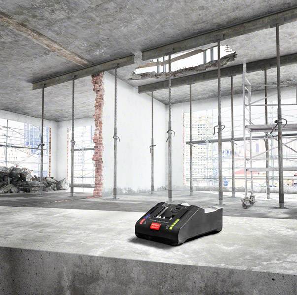 A construction site room with exposed walls, ceiling in progress. In the foreground, a digital measuring device on concrete.