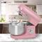 Pink stand mixer with mixing bowl and mixer attachment on a light-coloured kitchen worktop. Blurred kitchen furniture in the background.