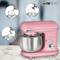A pink stand mixer with a stainless steel bowl and 1100W power. Three attachments shown: whisk, dough hook, and beater.