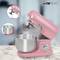 Pink stand mixer with mixing bowl and whisk attachment placed on a worktop. Brand name visible on the top of the machine.