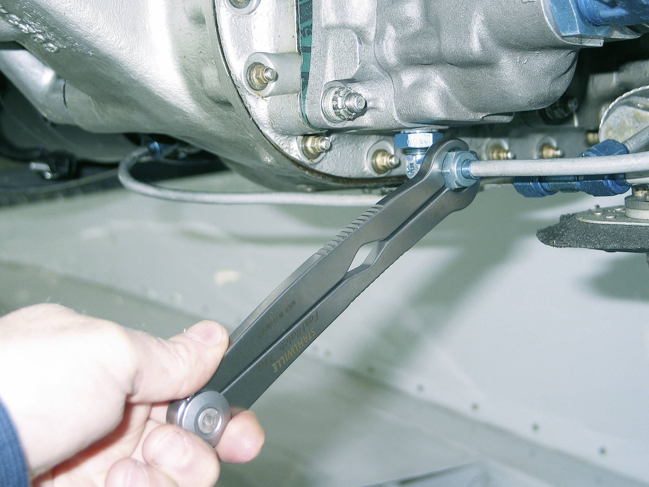 A hand is holding a spanner, which is positioned on a screw beneath a metal component. It appears to be a repair or maintenance task.