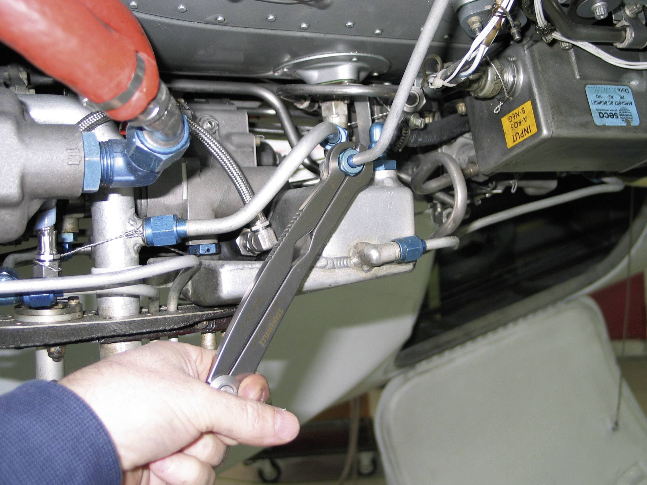 A person is repairing an aircraft engine with a spanner. Focus is on the hand and the tool on the metal component.