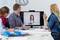 Three people in an office are conducting a video conference with a person on the screen. Everyone appears cheerful and engaged.