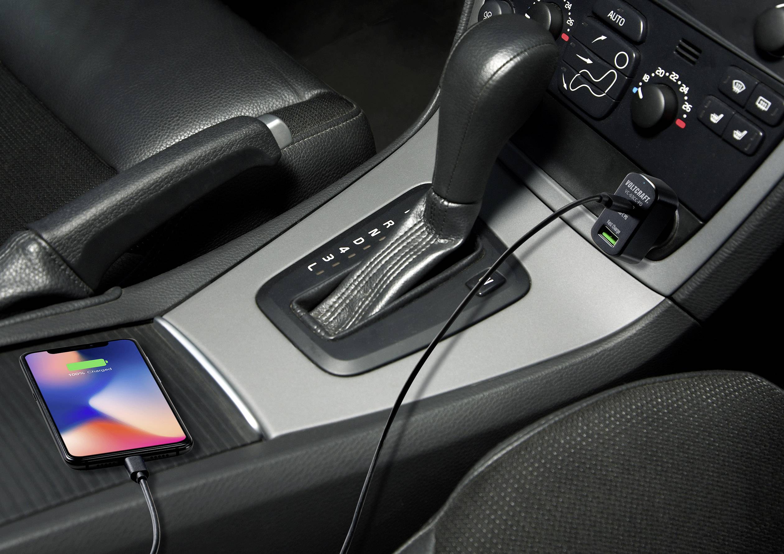 A mobile phone is being charged in the car. It is connected to the USB socket next to the gear stick via a cable.