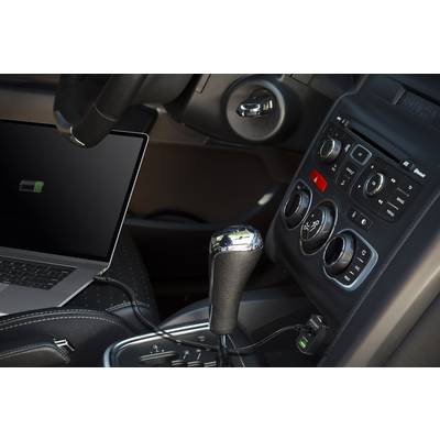 A laptop is charging in the car, connected to the dashboard. The steering wheel, centre console, and gear lever are visible.