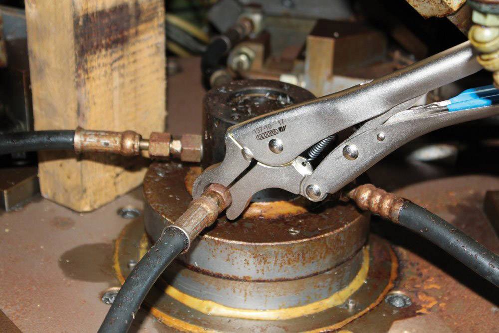 A spanner holds a pipe fitting on a metallic machine part that is connected to several hoses.