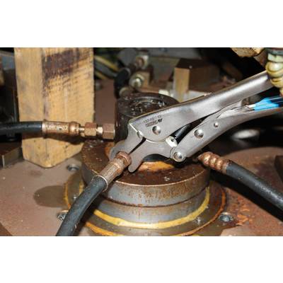 A metal tool grips a pipe connection in an industrial machine. Screws and pipes are visible.