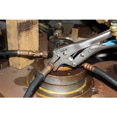 A pair of pliers holds a screw connection on a metal cylinder. Several hoses are connected to the cylinder.