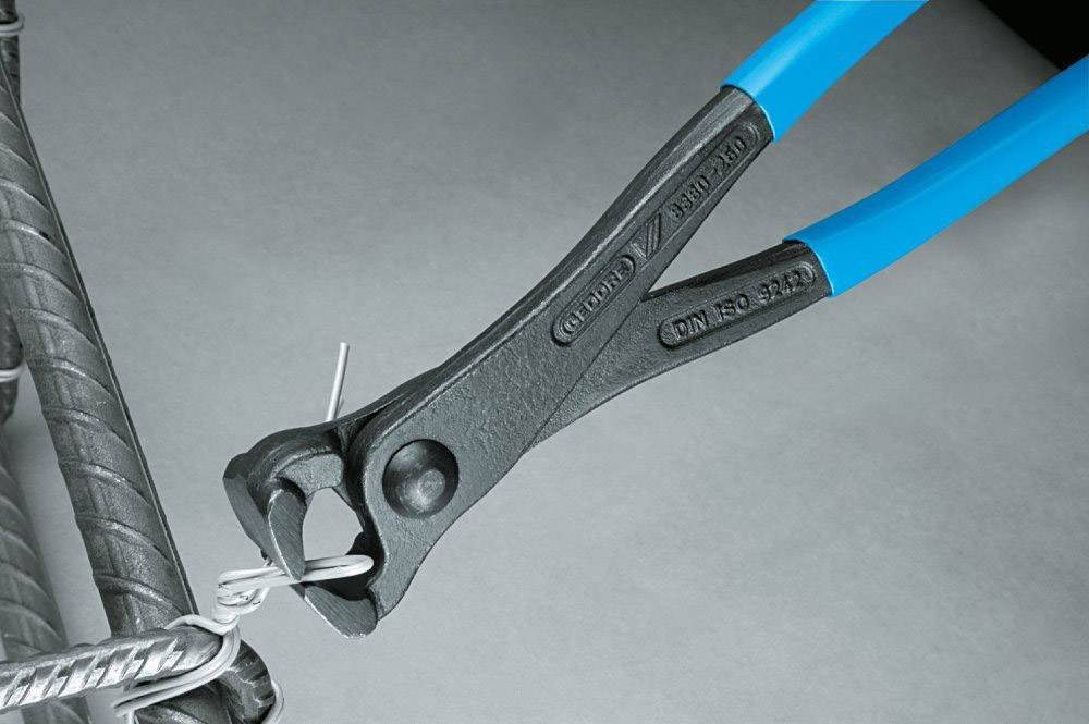 A pair of pliers with blue handles is cutting a thin wire attached to a metal frame.