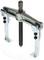 Two-legged metal puller with a central screw, standing on a glass plate. Tool for removing bearings or pulleys.