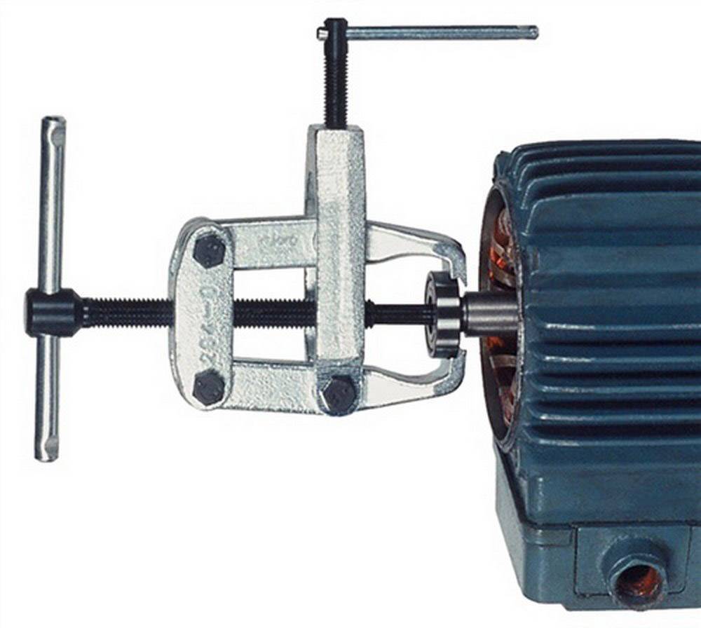 Close-up of a metal puller tool attached to the shaft of an electric motor to remove a component.