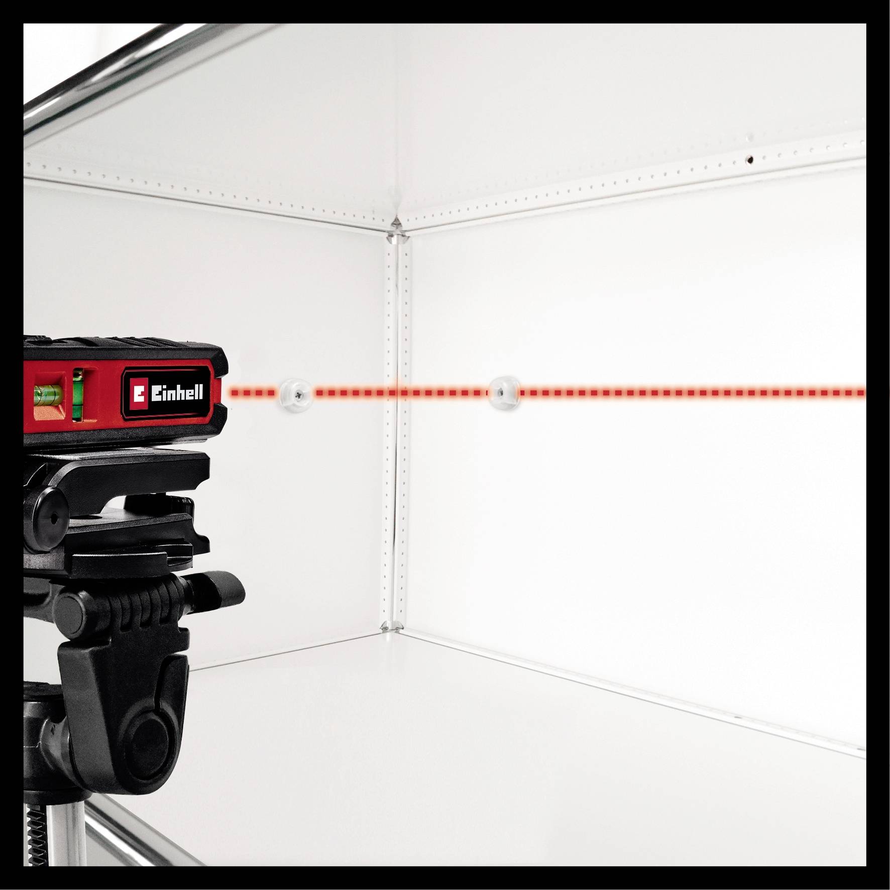 A laser levelling device illuminates a red line across a white surface. It is mounted on a tripod.