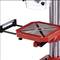 Industrial drilling machine with a red table and clamping fixture for securing workpieces. Function: Machining metal or wood.