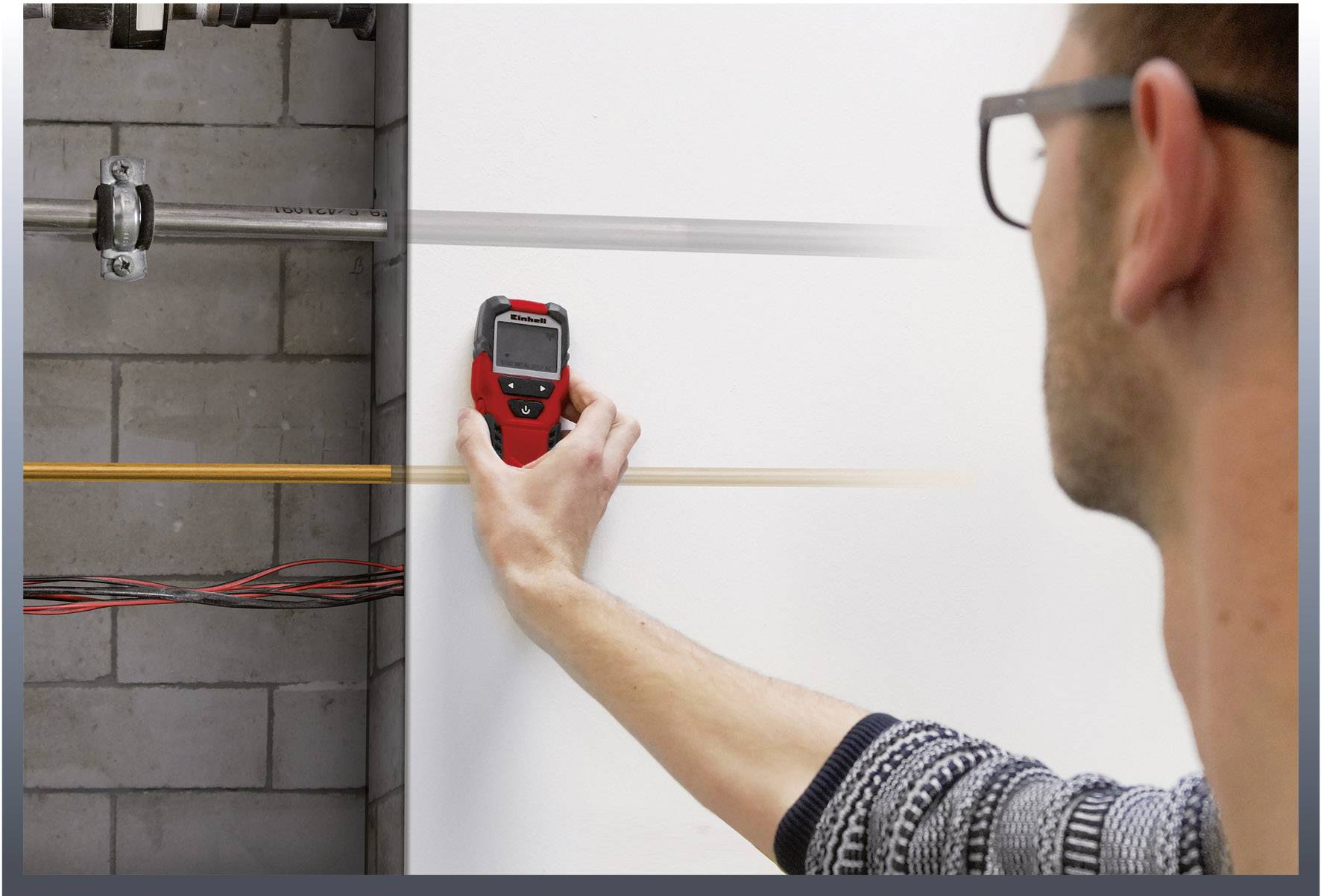 A man is using a digital detector on a wall to locate pipes. Visible cables and pipelines are present on the left side.