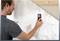 A man is testing the thickness or density of a wall using an electronic measuring device, possibly during renovation work.