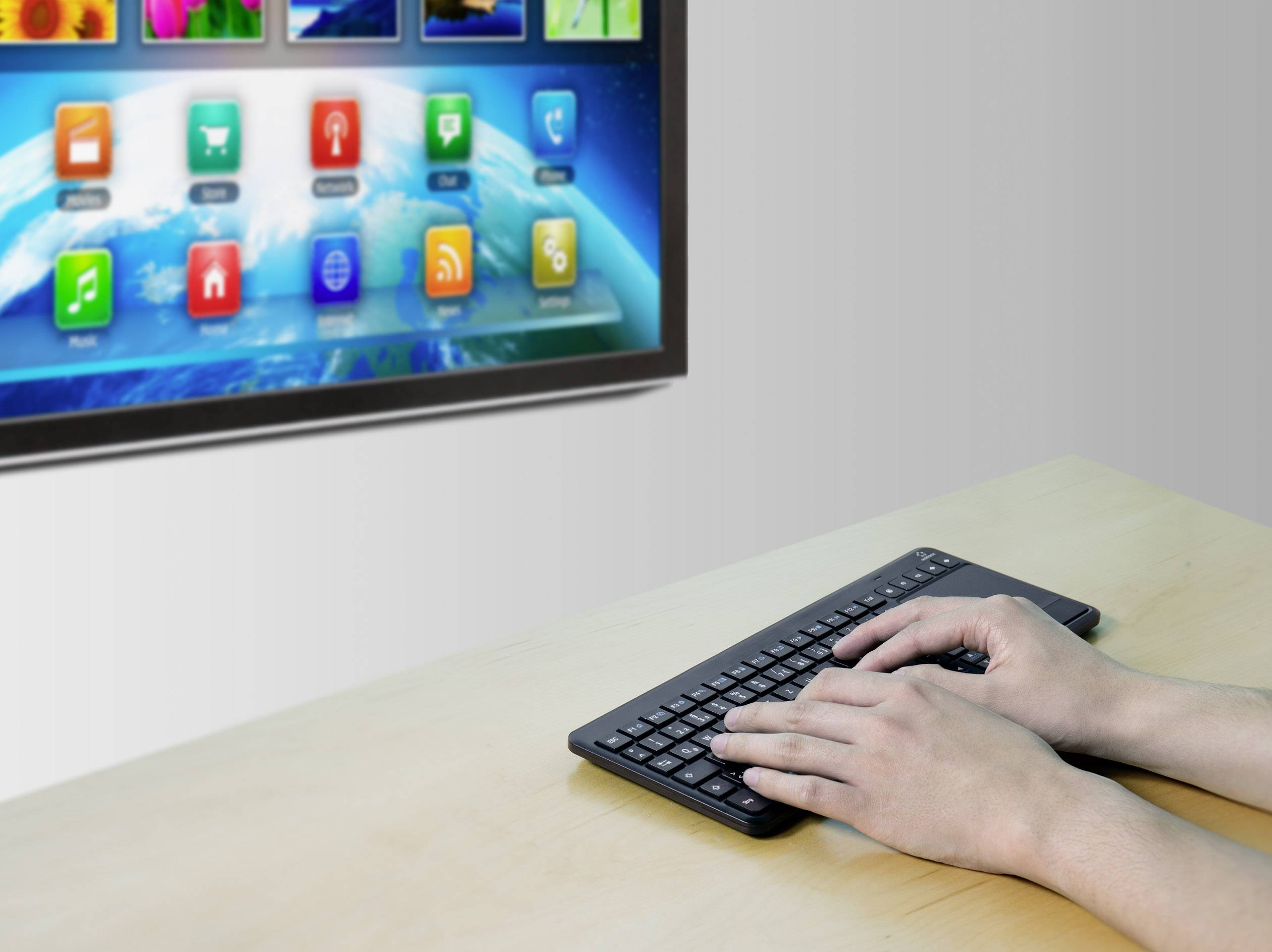 A person is typing on a wireless keyboard with a screen in the background displaying colourful, square app icons.