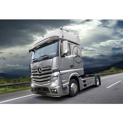 A silver lorry drives alone on an empty motorway with a cloudy sky in the background.