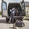 A tradesman is working at the open boot of a van. A tool bag is standing on the ground in the foreground.