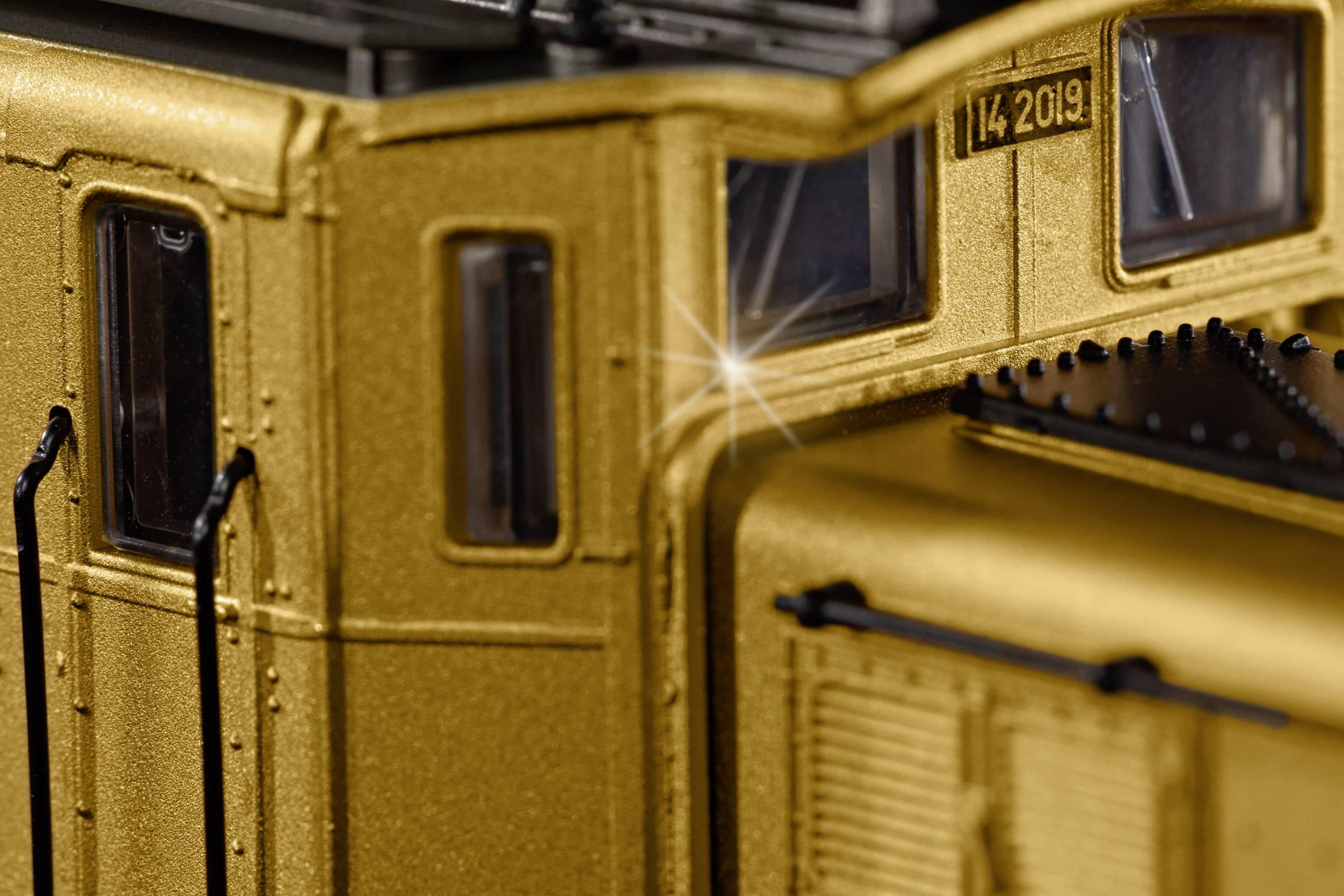 Close-up of a golden model railway carriage with sparkling light on its surface, showcasing the detail and precision of the construction.