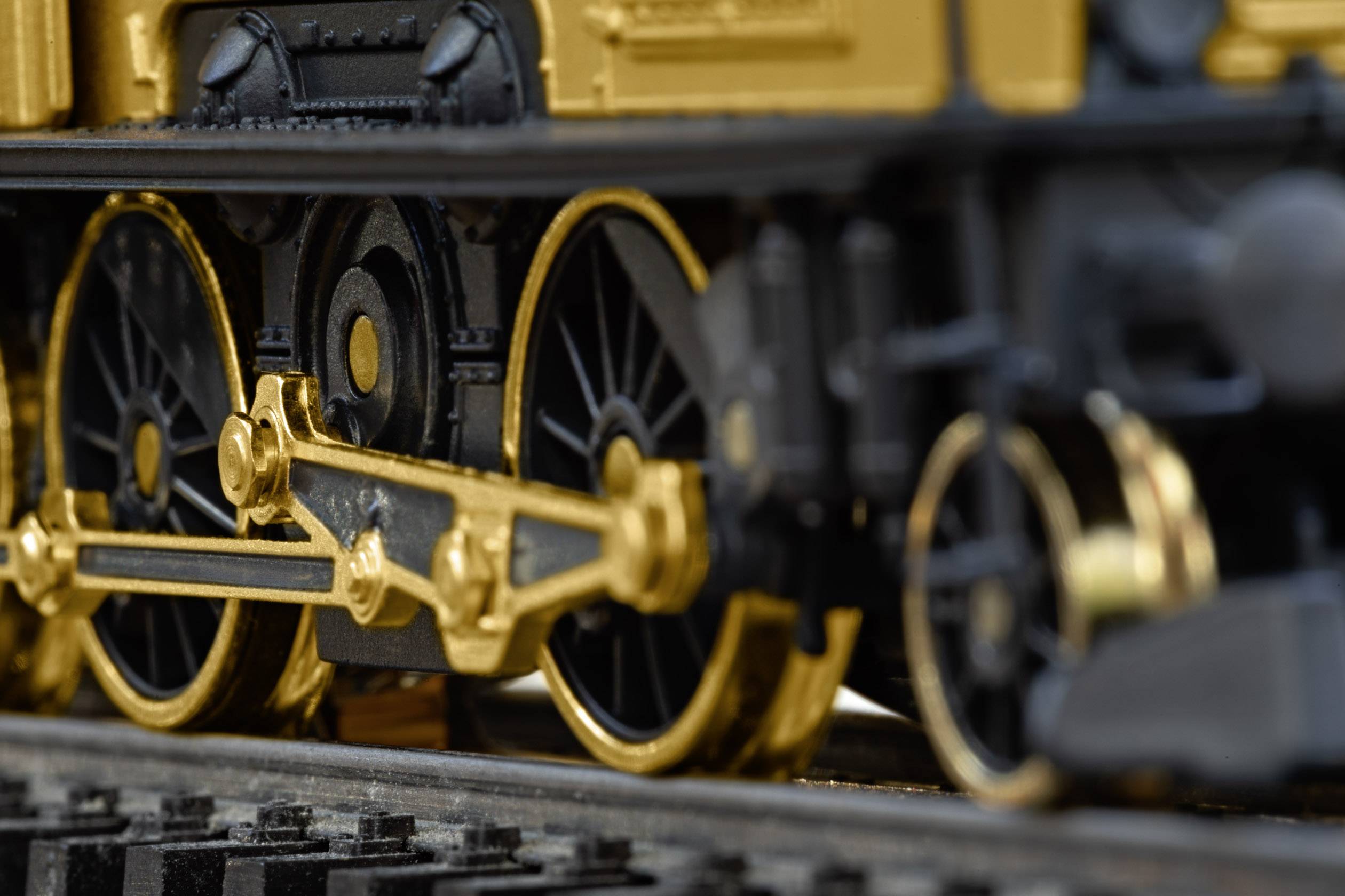 Close-up of golden and black wheels of a historic train model on rails.