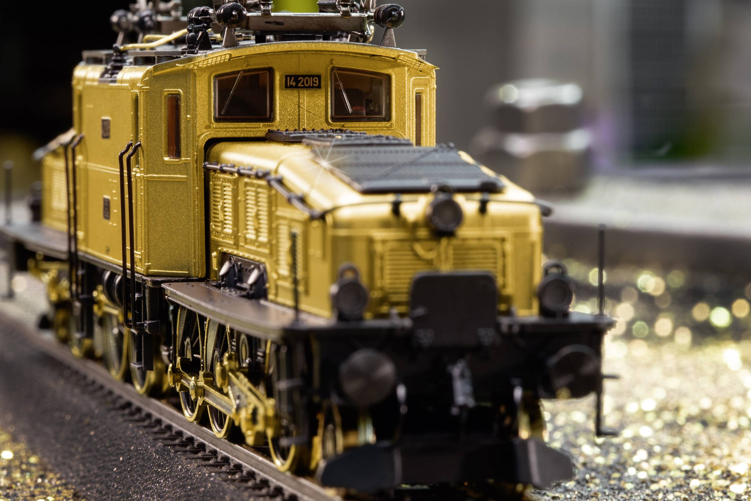 A detailed model of a gold-coloured steam locomotive on railway tracks, surrounded by glittering particles.