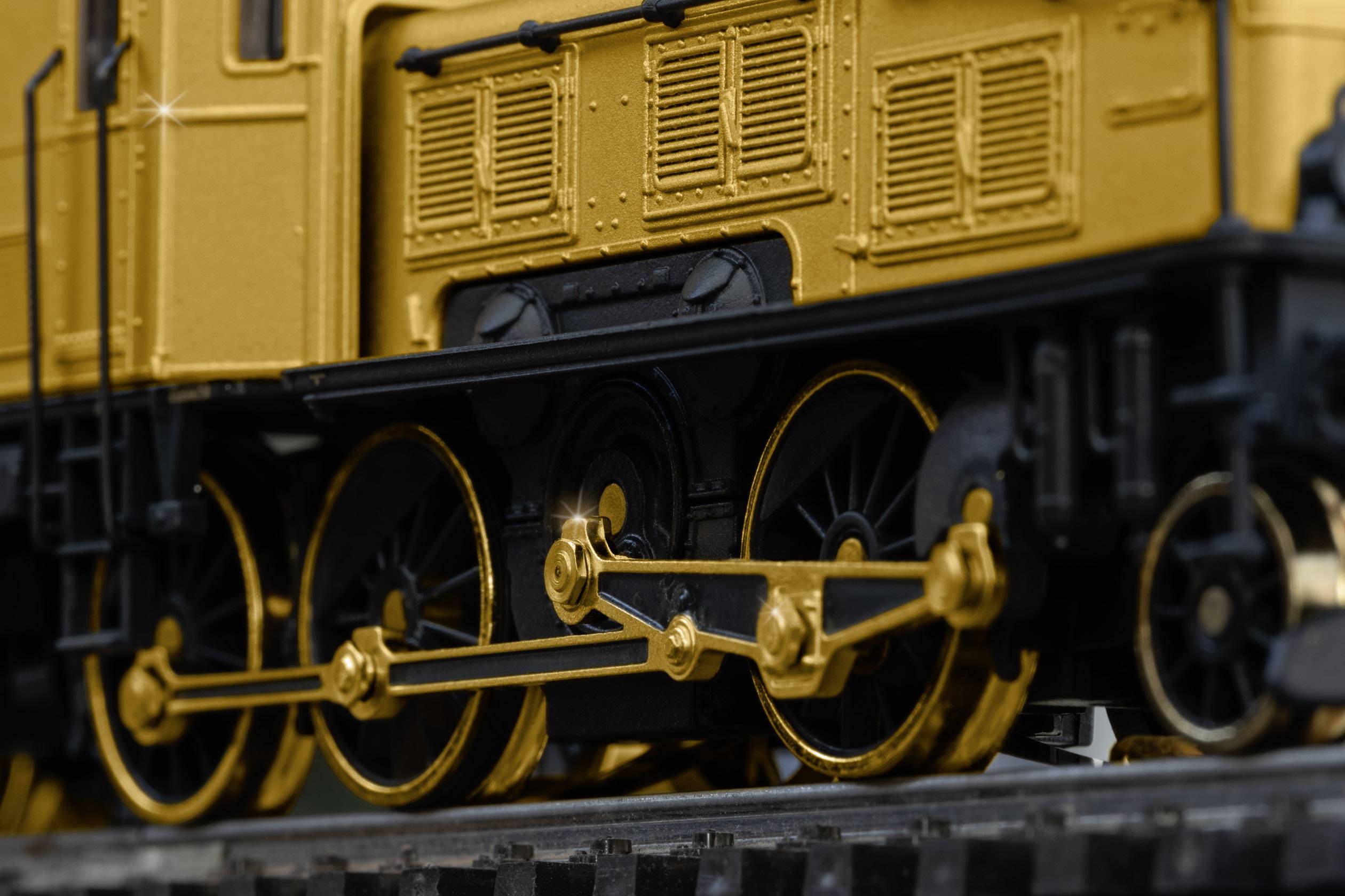 Close-up of a gold-coloured model train, showing the detailed craftsmanship of the wheels and axles on the tracks.
