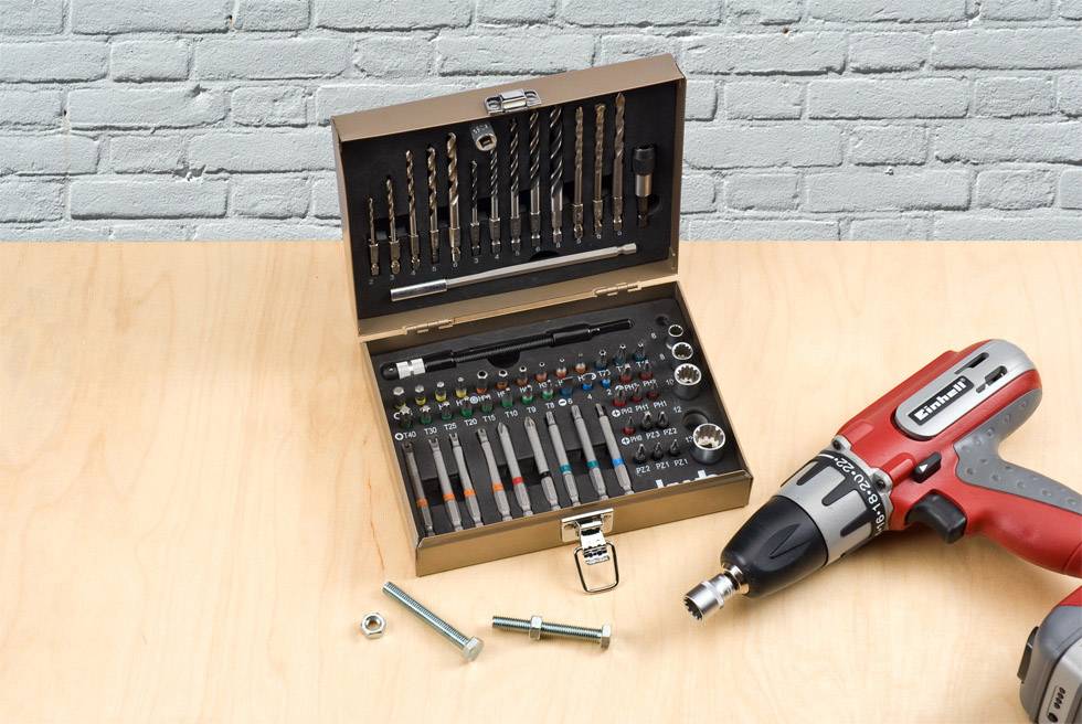 Tool case with drill bits and screwdriver attachments, open on a table next to a red, cordless power drill.